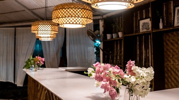 Una zona de bar con paneles de madera, lámparas de mimbre colgantes y centros de mesa florales sobre una encimera de mármol.