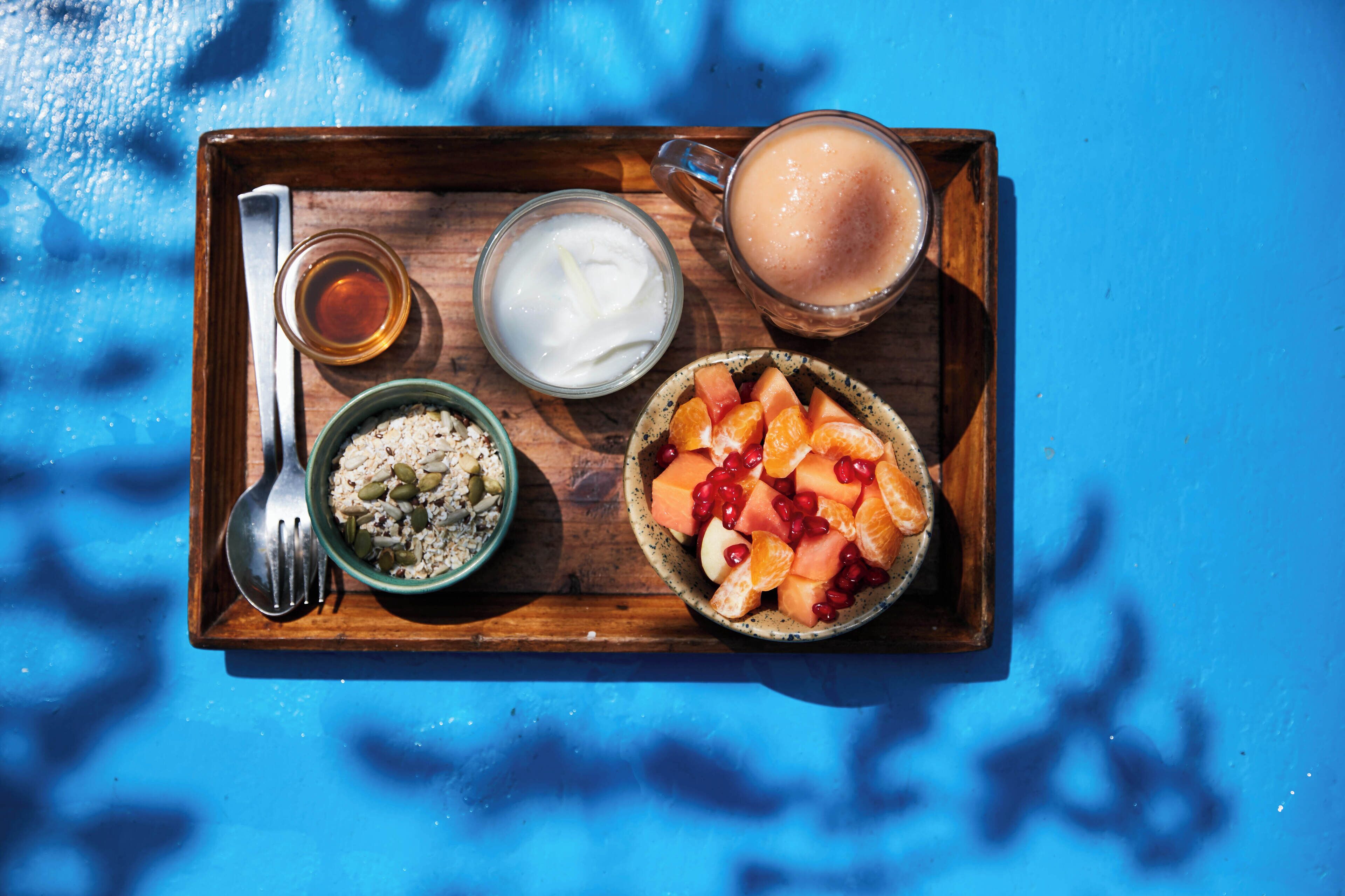 A wooden tray with food items including a bowl of rice, a bowl of fruit, a glass of milk, and a mug of coffee.
