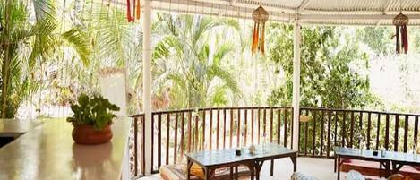 An outdoor covered patio with a table and benches, surrounded by lush greenery.