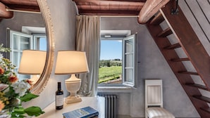 A room with a window, a radiator, a chair, a table with a lamp and a book, and a bottle. - Tenuta Guardastelle (San Gimignano)