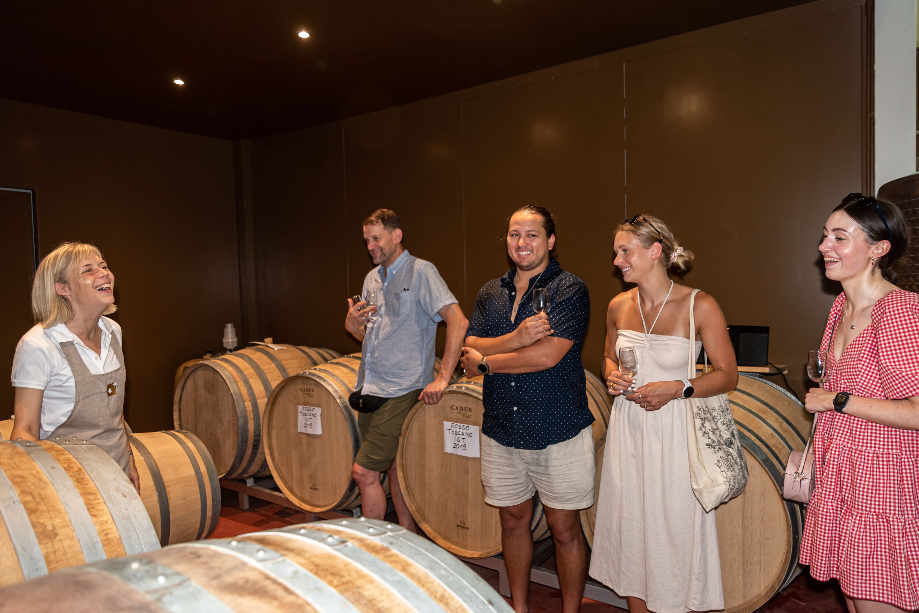A group of people standing in a room with wooden barrels, likely a wine cellar or tasting room.