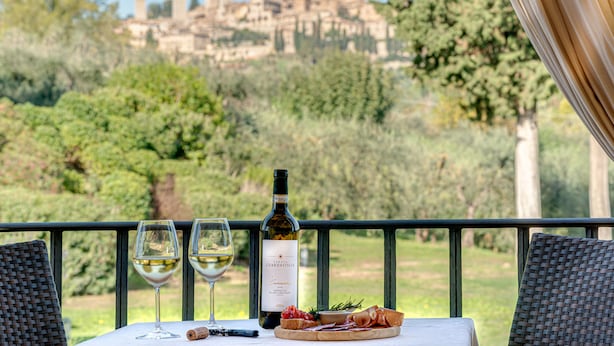 A table with a bottle of wine, two glasses, and a plate of food on a balcony overlooking a historic cityscape. - Tenuta Guardastelle (San Gimignano)