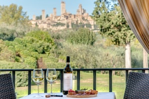 A table with a bottle of wine, two glasses, and a plate of food on a balcony overlooking a historic cityscape. - Tenuta Guardastelle (San Gimignano)