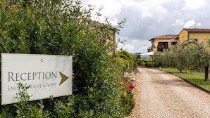 A reception sign for a taste and shop, surrounded by greenery and a gravel path leading to buildings. - Tenuta Guardastelle (San Gimignano)