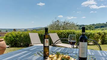 Una mesa con dos botellas de vino y una copa de vino tinto, una tabla de madera con comida, y una vista panorámica de fondo.