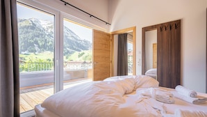 Un dormitorio con una cama grande, una puerta de madera que da a un balcón y vistas a las montañas.