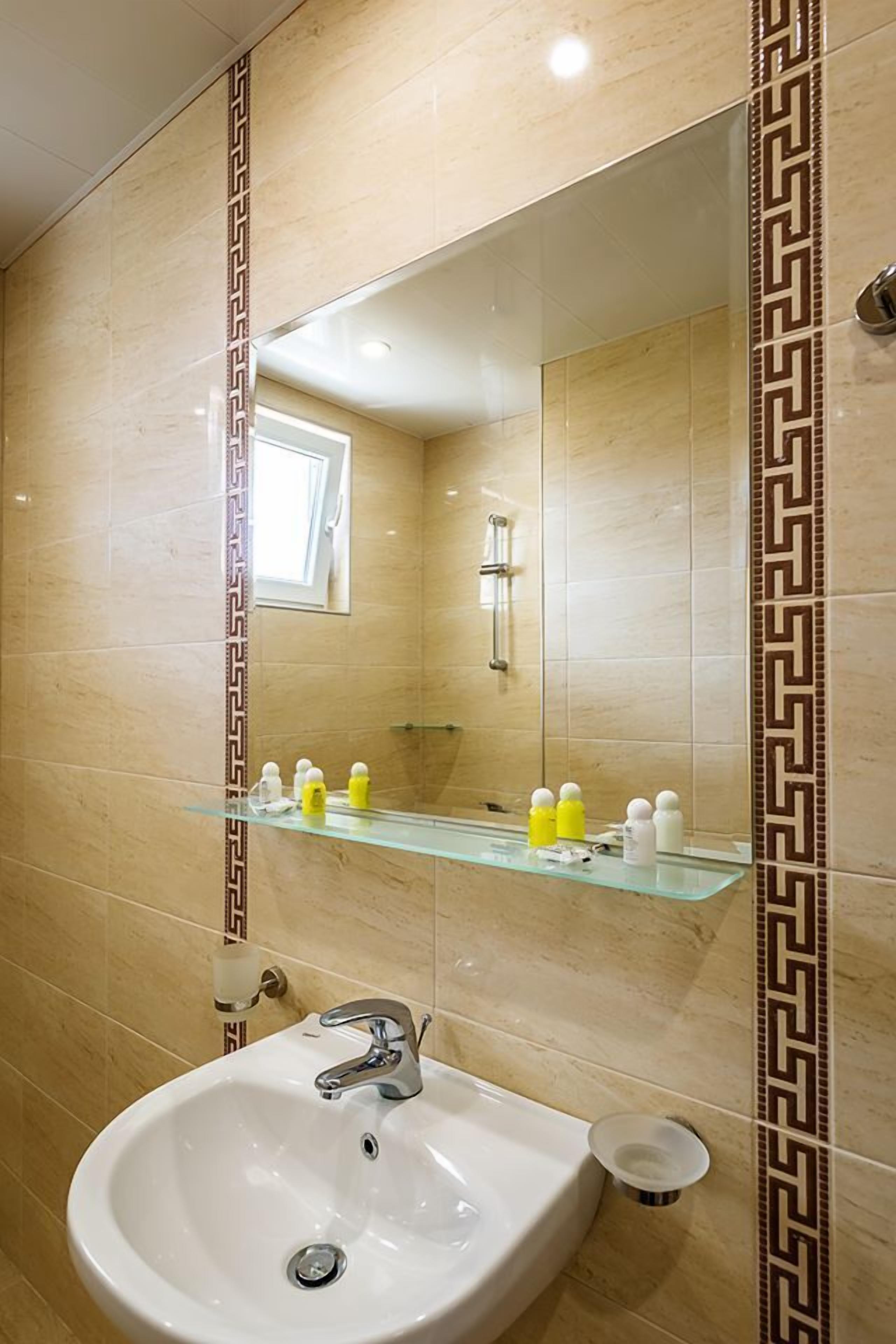Un baño con lavamanos blanco, un espejo y una repisa de vidrio con artículos de aseo.