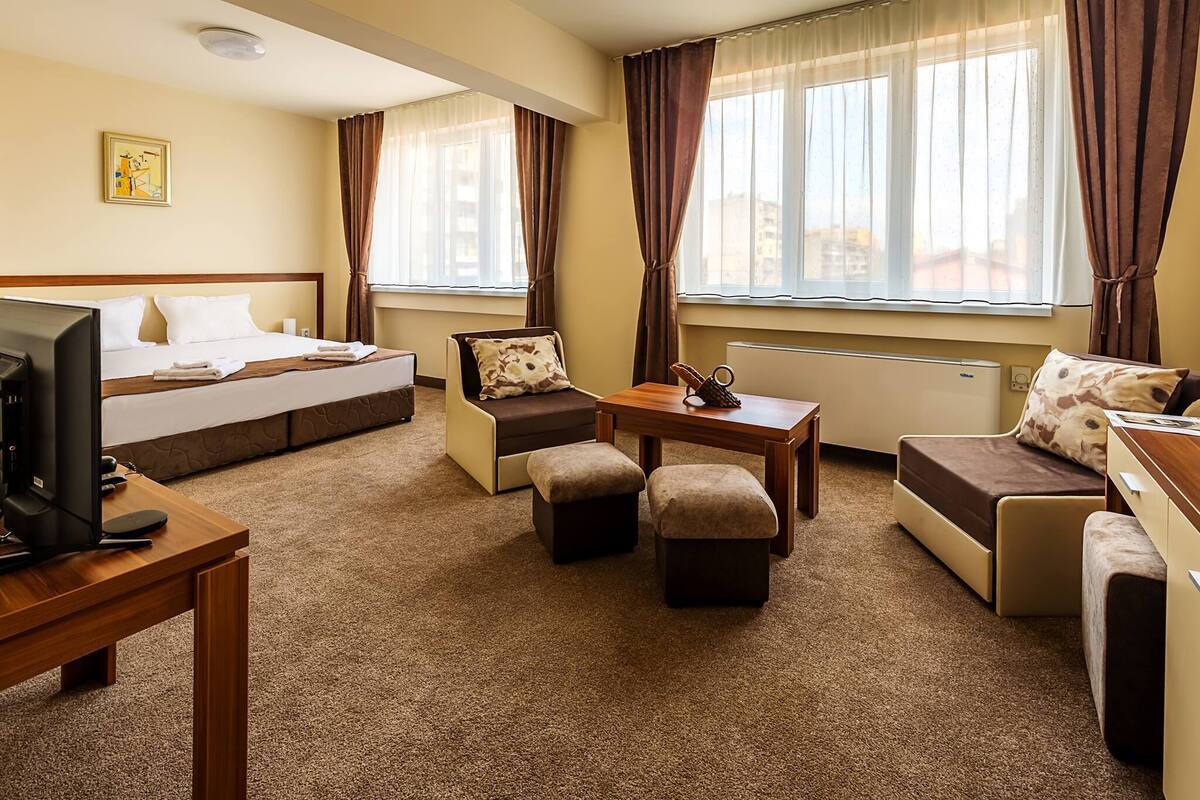 A hotel room with a bed, a desk with a computer, a sofa, a small table, and a chair.