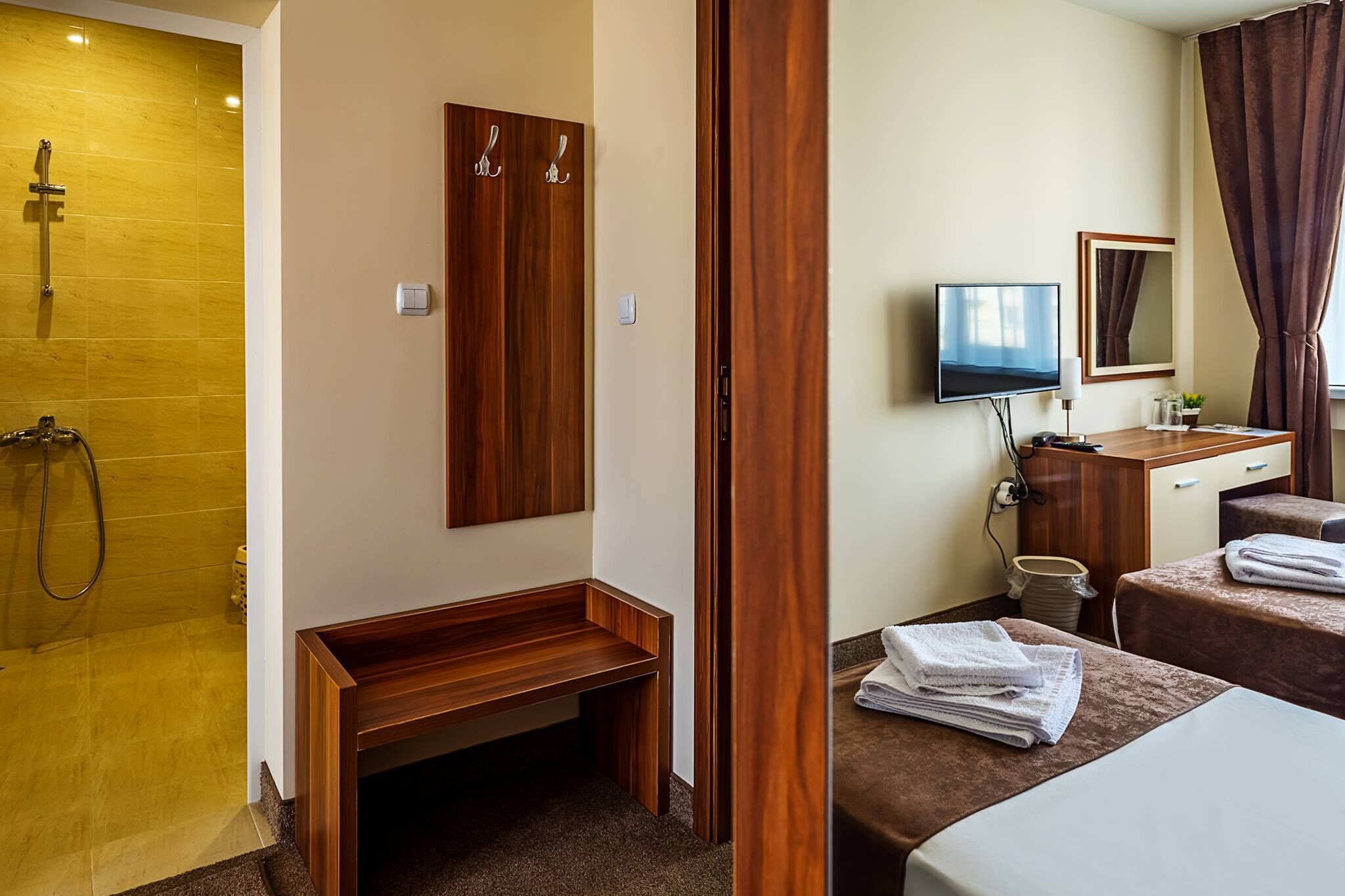 A hotel room with a wooden bench, a TV, a mirror, and towels on the bed.