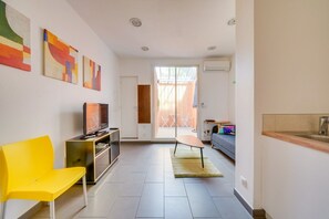 Un salon moderne avec un téléviseur, un fauteuil jaune et des œuvres d’art accrochées au mur.