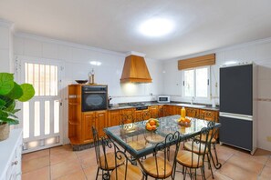 A kitchen with wooden cabinets, a glass dining table, and a black refrigerator. - Fidalsa Divine Hiding (Algorfa)