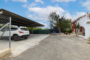 A parking area with a white SUV, a covered carport, a swing set, and a building with a red facade. - Fidalsa Divine Hiding (Algorfa)