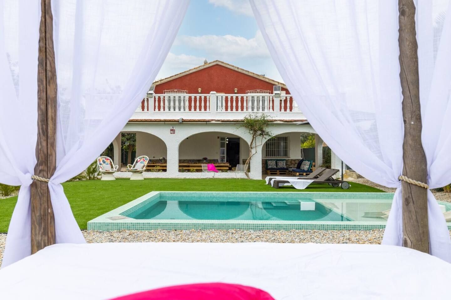 Vista de la piscina de una casa con techo rojo, barandillas de balcón blancas y una piscina azul cristalina.