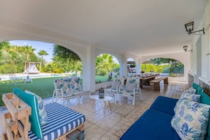 A covered outdoor seating area with a pool view, wooden furniture, and a dining table set for four. - Fidalsa Divine Hiding (Algorfa)