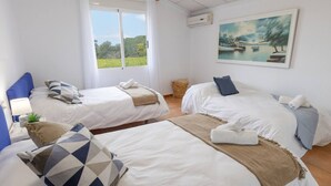 Quarto de hotel com duas camas, um quadro e vista para o verde.