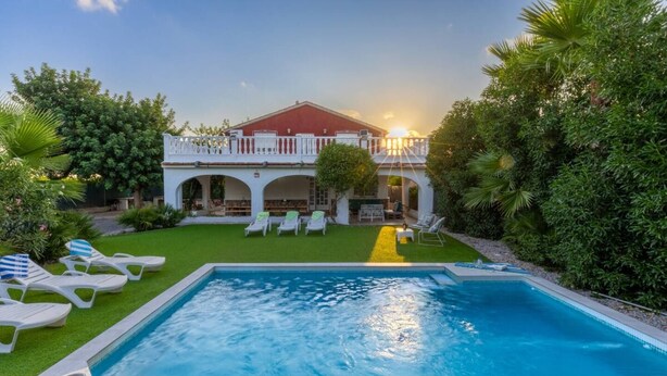 Piscina com espreguiçadeiras e um edifício com telhado vermelho e varanda branca.