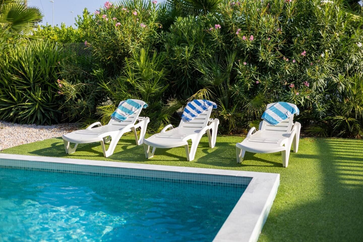 A poolside area with three white lounge chairs, each with a striped towel.