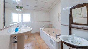Casa de banho com uma banheira grande, lavatório e espelho.