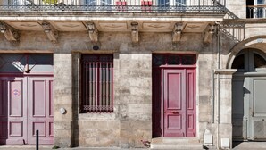 Un edificio con dos puertas rojas y una ventana con barrotes, que presenta arquitectura de piedra y un pequeño balcón.