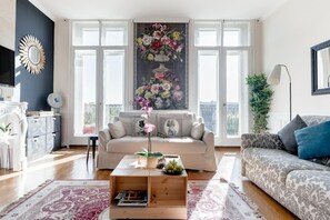 A spacious living room with a large window, a sofa, a coffee table, and a decorative painting. - Nice apartment Bordeaux Chartrons with parking (Bordeaux)