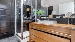 Un baño moderno con cabina de ducha de vidrio, tocador de madera con lavamanos y un espejo grande.