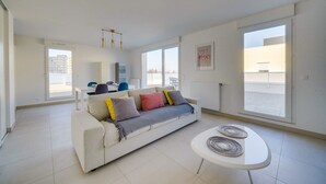 Una sala de estar moderna con un sofá blanco, una mesita redonda y grandes ventanales con vistas a la ciudad.