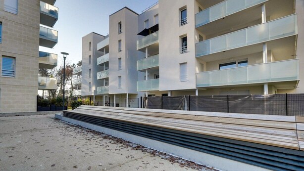 Un moderno edificio de apartamentos con varios balcones, un espacio al aire libre cubierto y suelo de arena.