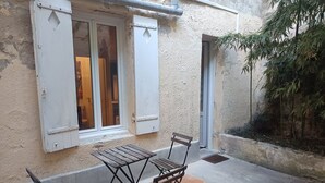 An outdoor seating area with a table and chairs, a window with shutters, and a door. - Charming apartment downtown Bordeaux (Bordeaux)