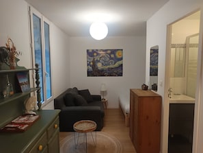 Un espace de vie compact comprenant un canapé, une petite table, une lampe, un meuble en bois et un tableau accroché au mur.