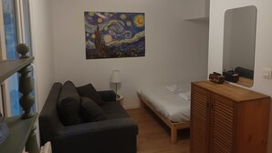 A bedroom with a bed, a wooden wardrobe, a nightstand with a lamp, a painting on the wall, and a window with blinds. - Charming apartment downtown Bordeaux (Bordeaux)