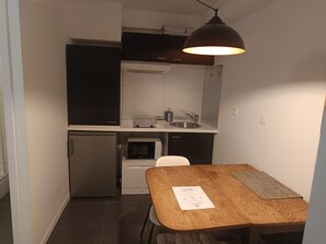 Cocina compacta con microondas integrado, un refrigerador pequeño y un lavabo. Hay una mesa de madera con un tapete de bienvenida y un papel encima.