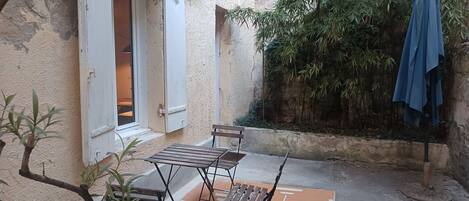A courtyard with a table and chairs, a door, and a blue umbrella.