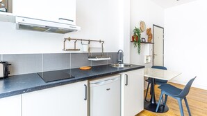 Eine kompakte Küche mit schwarzer Arbeitsplatte, weißen Schränken, einem eingebauten Backofen und einem kleinen Kühlschrank. Es gibt ein Spülbecken mit Armatur, einen Hängevorrat und einen Esstisch mit Stühlen.