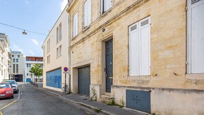 A narrow street with parked cars and a building with a stone facade and white shutters.