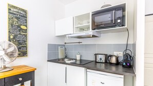 A compact kitchen with a microwave, toaster, kettle, and a fan.
