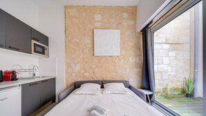 A modern bedroom with a large bed, a built-in microwave, a small kitchen area, and a view of the courtyard.