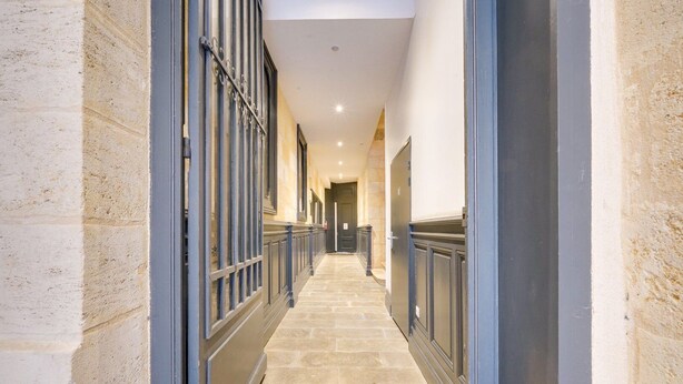 A corridor with stone walls, metal railings, and doors leading to rooms.