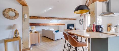 Une cuisine moderne avec un plafond en bois, un coin repas doté d’une grande table et de chaises, et un salon avec un canapé et un téléviseur.