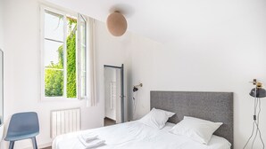 A bedroom with a bed, a chair, a table, and a window with a view of greenery. - Beautiful apartment Bordeaux center (Bordeaux)