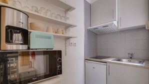 A compact kitchen with a microwave, toaster, and dishwasher. There are shelves above the counter holding glass jars and plates.