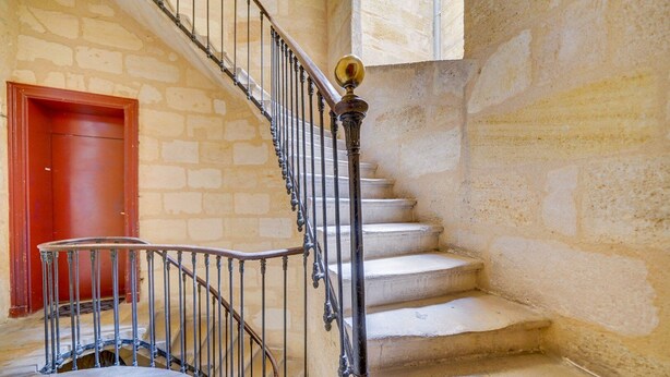 A stone staircase with a metal railing and a red door at the top.