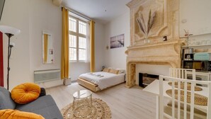 A modern bedroom with a bed, a fireplace, a dining area, and a large window with curtains.
