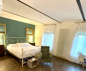 A bedroom with a bed, two chairs, a nightstand, a bedside table, and a window with curtains. - Lange (Priocca)