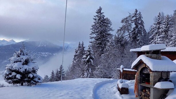 Paisagem montanhosa coberta de neve, com uma cabana de madeira e um teleférico.