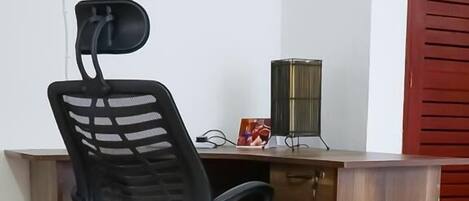 A corner office with a black office chair, a wooden desk, a red door, and a tiled floor.