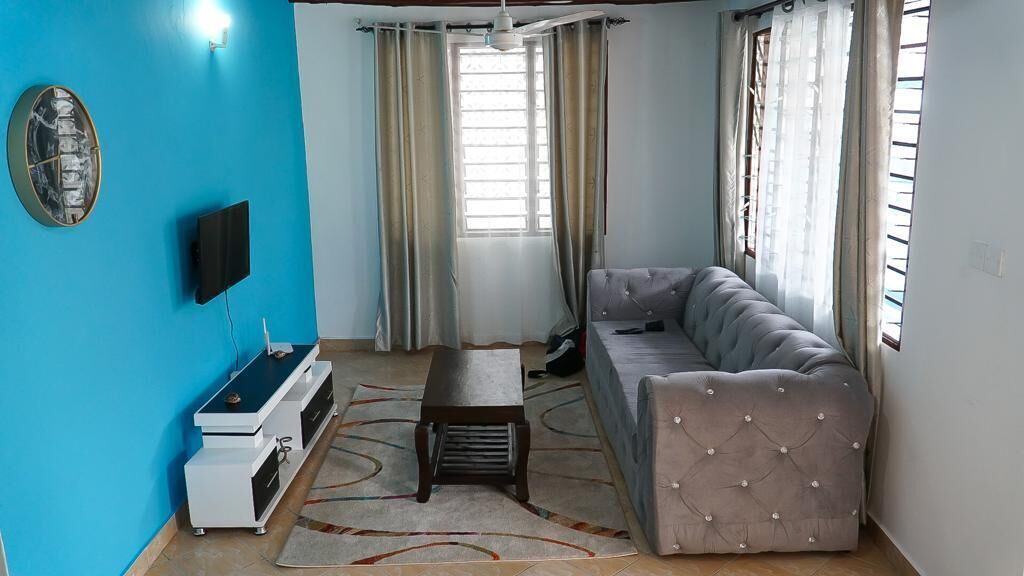 A living room with a sofa, a TV, a small table, and a decorative wall piece.