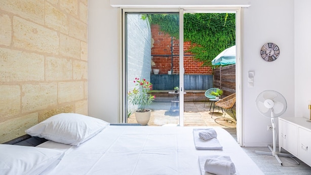 Un dormitorio con cama, puerta corrediza de vidrio a un patio, un ventilador y un reloj en la pared.