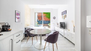 Un espacio habitable moderno y funcional con cocina, comedor y un pequeño balcón con pared de ladrillo y plantas.