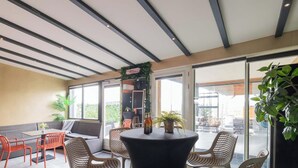 A modern indoor seating area with a high ceiling, glass doors leading outside, and a variety of seating options including a round table and chairs. - Amsterdam Villa | Jacuzzi, Sauna & Cinema (Zwanenburg)