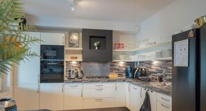 Una cocina moderna con armarios blancos, un horno Bosch, una cafetera y una campana extractora negra.